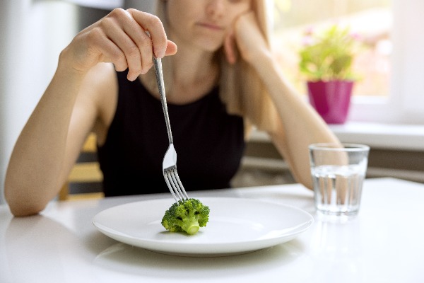 white female sitting at a table with broccoli on her plate